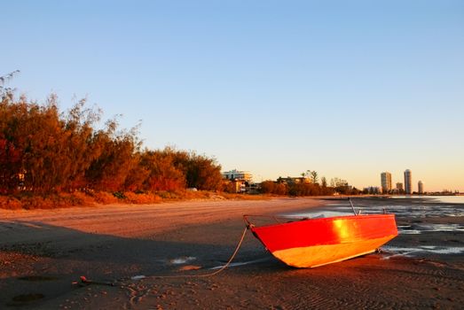 Red dinghy on the beach at sunrise at Labrador looking toward Runaway Bay, Gold Coast Australia.