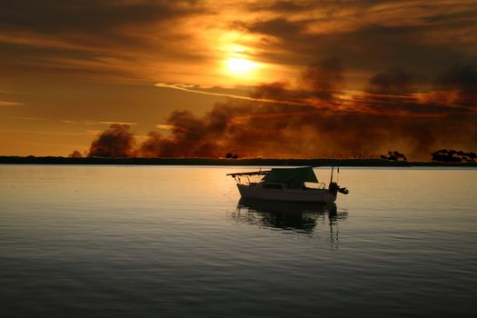 Sailing boat moored with a wild fire burning in the background.