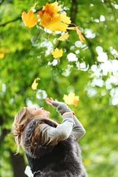 woman drop up leaves in autumn park