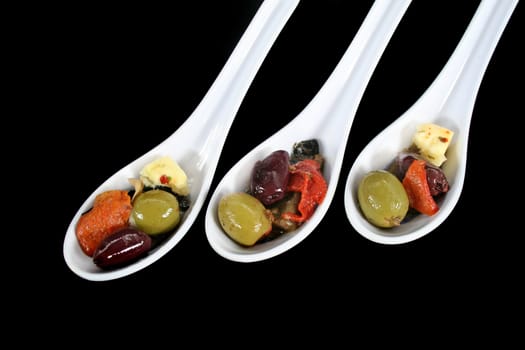 Three antipasto spoons filled with olives, cheese and goodies.