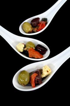 Three antipasto spoons filled with olives, feta cheese and goodies.