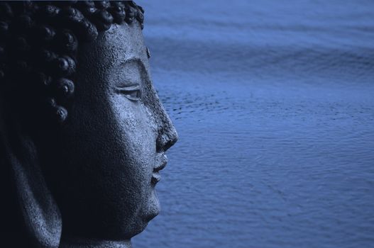 A Buddha statue in blue agains a beautiful blue ocean with ripples