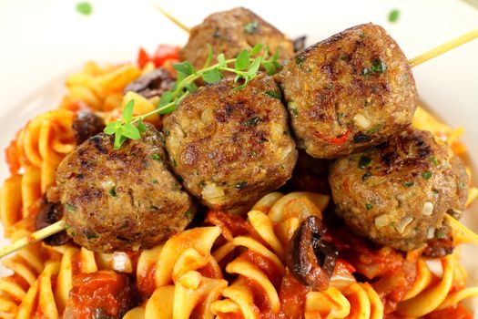 Delicious skewered beef meatballs on tomato and olive pasta.