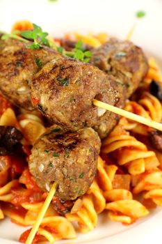 Delicious skewered beef meatballs on tomato and olive pasta.