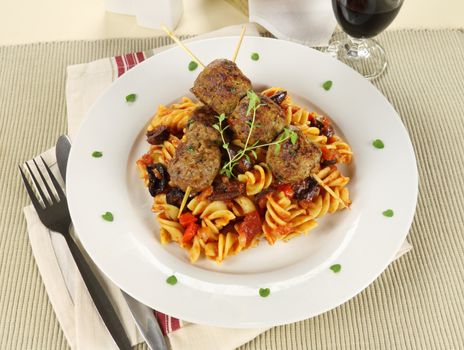 Delicious beef meatballs on tomato and olive pasta with bread and wine.