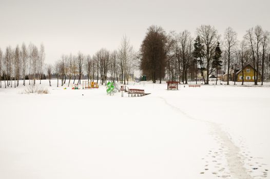 footpath through frozen lake and summer beach playground covered with snow in winter season.