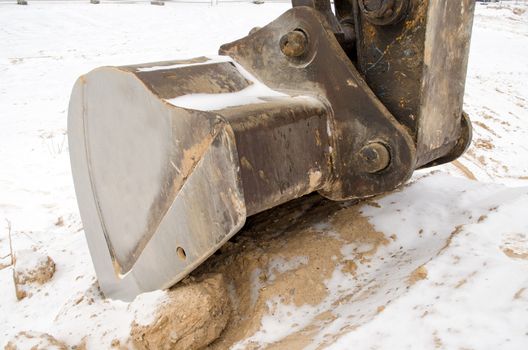 excavator bucket closeup in sand pit quarry covered with snow in winter.