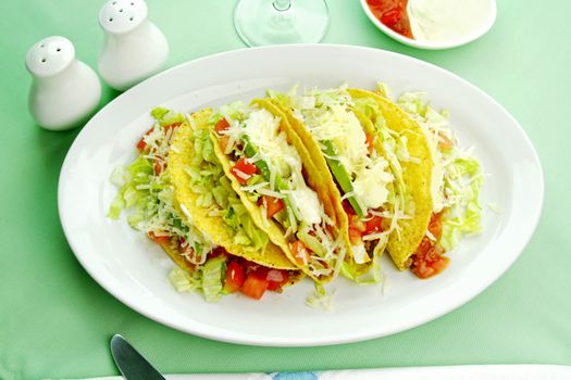 Delicious beef tacos with beef, lettuce, tomato salsa, avocado, grated cheese and sour cream.