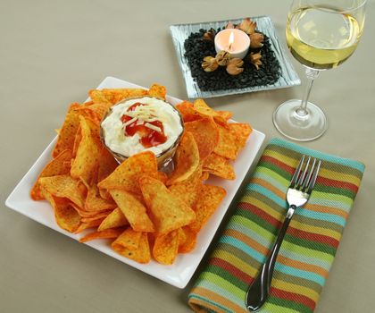 Nachos and Mexican dip topped with sour cream, salsa and grated cheese with copy space top left.