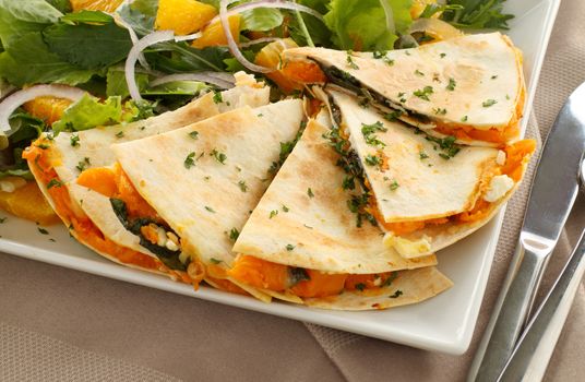 Delicious pumpkin quesadilla sliced and ready to serve with a garden salad.