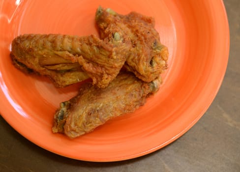 crispy fried chicken wings on an orange plate and a wooden background