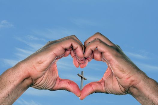 Jesus is love concept with a pair of hands in a heart shape holding a cross against a blue sky