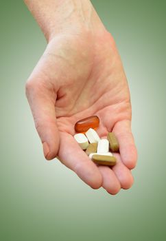 hand holding daily supplements, vitamins or medication on green background