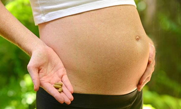 pregnant woman holding prenatal vitamins by stomach