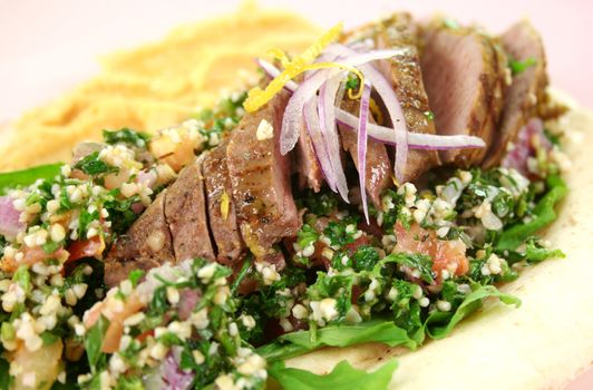 Sliced Middle Eastern lamb fillet with hummus and tabouleh.
