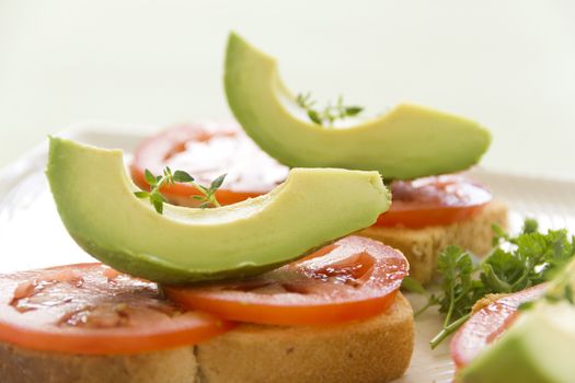 Delicious fresh slice of avocado with tomato and thyme on sliced toasts.