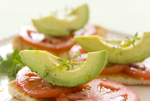 Delicious fresh slice of avocado with tomato and thyme with ground pepper on sliced toasts.