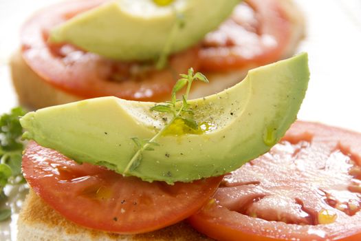Delicious fresh slice of avocado with tomato and thyme with ground pepper on sliced toasts.