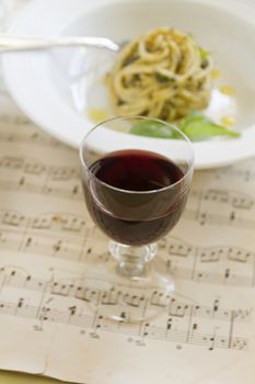 Red wine with pesto spaghetti on an old music sheet.