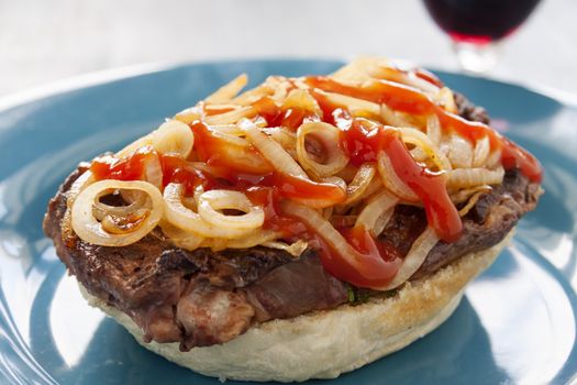 Freshly prepared open fillet steak burger with fried onions and ketchup ready to serve.
