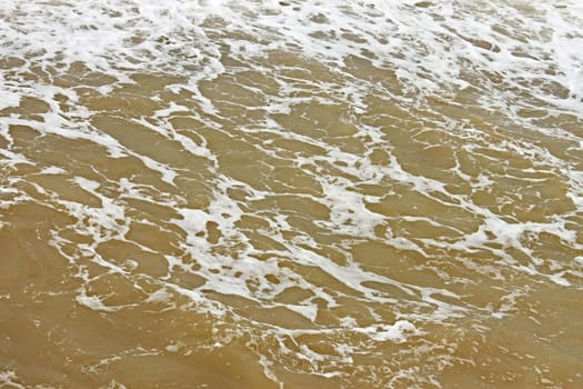 Coastal foamy seawater surface after the storm polluted dredged from the seabed sand