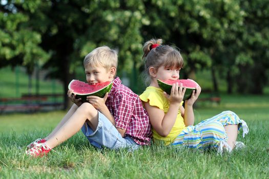 boy and little girl sitting on grass and eat watermelon