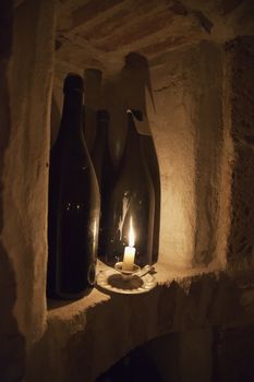A candle near two bottles of wine in a cellar