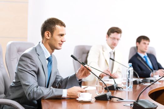 Portrait of a businessman, said into the microphone, in the background colleagues communicate with each other