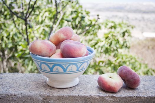 A ceramic bowl with donut peaches, so called peento, in a garden