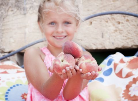A smiling child holding out flat peaches, so called peento. Blurred background