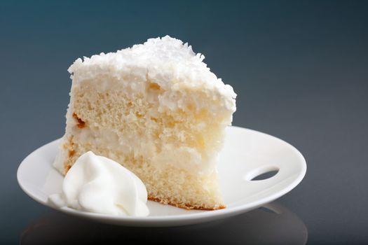 A fresh piece of coconut cream cake on a white plate with a bit of whipped cream on the side.