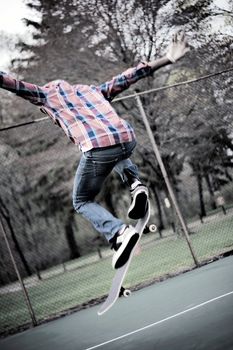 A skateboarder performs tricks in some tennis courts.