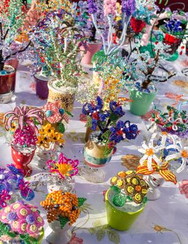 various decorative handmade artificial flowers in pots made of small plastic colorful beads sale in market fair.