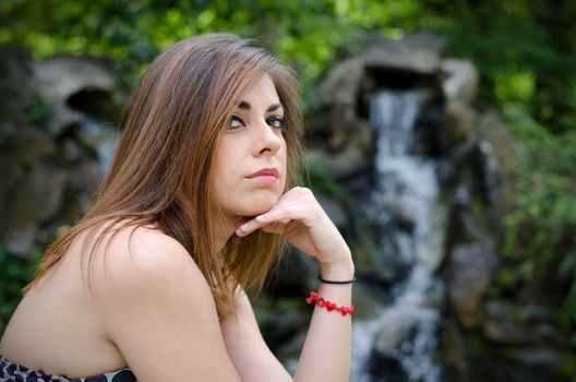 Pretty girl sitting and looking in camera, outdoors with small waterfall behind her