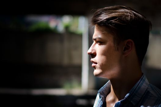 Profile of attractive young man in urban setting, lit by a ray of sunlight