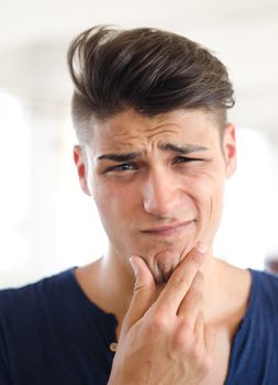 Unsure, confused, puzzled young man looking in camera with hand on his chin, thinking