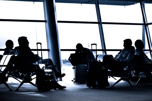 Silhouettes of business people traveling on airport; waiting at the plane boarding gates.