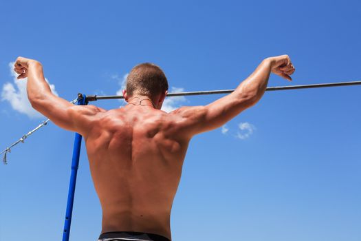 Young strong athlete standing before horizontal bar against blue sky