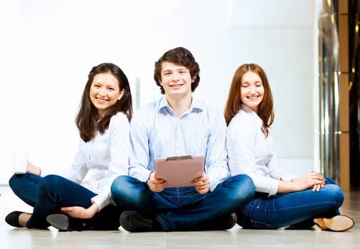 Image of three students in casual wear sitting on floor and smiling