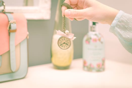 Beautiful girl hand holding a small vintage clock necklace in front of female complements in soft pastel colors