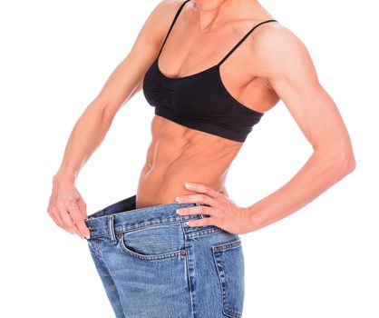 Muscled woman shows her weight loss by wearing the old jeans, isolated on white background