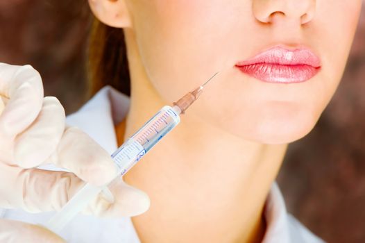 hand in glove holding syringe with botox pointed at a right corner female lip. Focus on syringe.