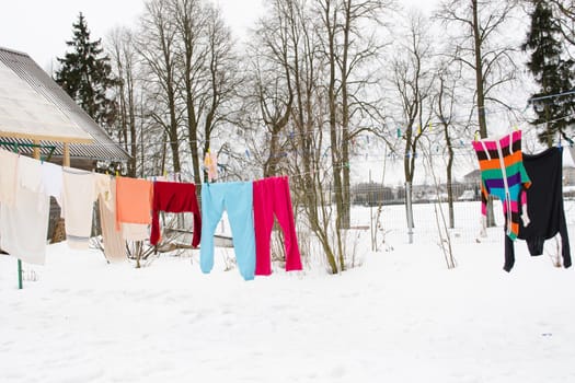 colorful washed wet clothes loundry dry hang on rope in house yard in winter.