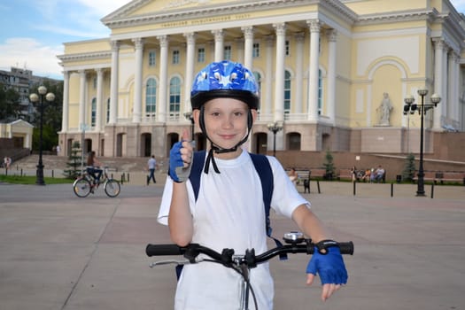 The happy teenager by bicycle near the Tyumen drama theater shows an approval sign.