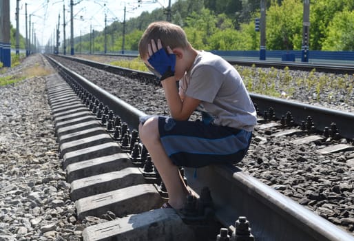 the sad boy sits on rails, having clasped the head hands