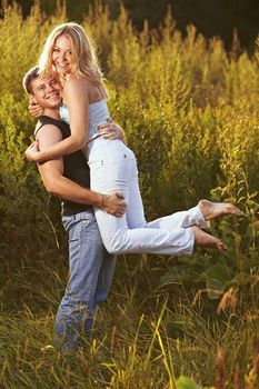 Young couple on the background of the high grass. The guy holding the girl in his arms