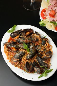 Mussels dinner with red sauce and pasta and an antipasto salad.  Shallow depth of field.