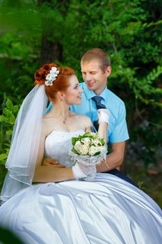 Portrait of happy newlyweds in a city park. Bride is holding a tie for the groom