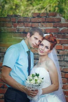 Portrait of Happy Newlyweds in a City Park on a Background of a brick wall