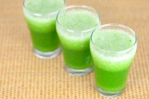 three glasses with celery juice on wooden mat